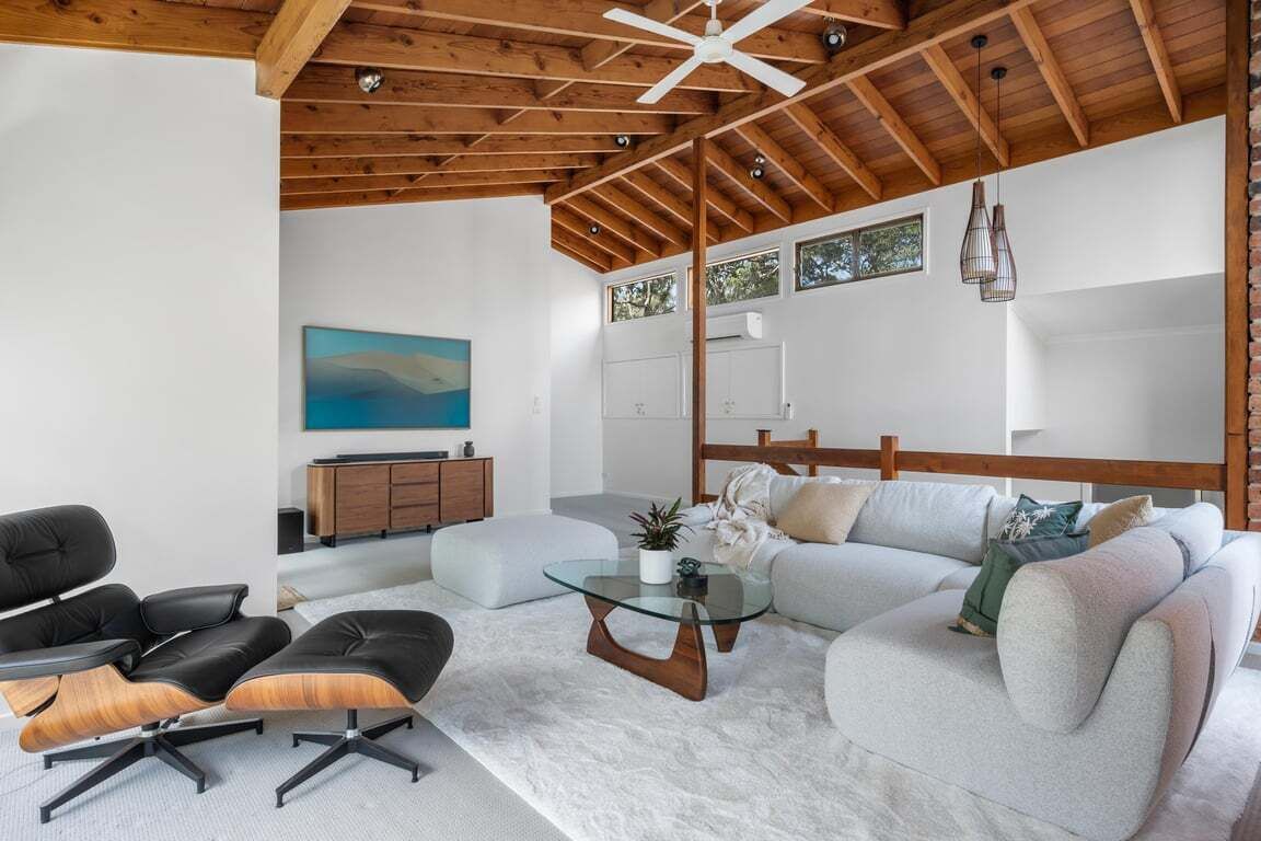 Una sala moderna con techo alto, un conjunto de sofás, una mesa de centro de vidrio y un aparador de madera.