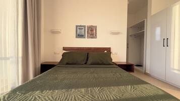 Ein ordentlich bezogenes Bett mit grüner Bettdecke, einem Holzkopfbrett und zwei Nachttischlampen. An der Wand über dem Bett hängen zwei gerahmte Bilder.