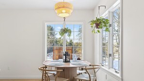 Un comedor con una mesa redonda de madera, cuatro sillas, un farol colgante y una ventana con vistas a árboles y una cerca de madera.