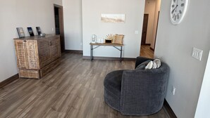 A living room with a grey armchair, a wooden cabinet, and a small table with decorative items. - Spacious 2 bedroom condo on Lake Kampeska (Watertown)