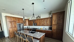 A kitchen with wooden cabinets, a granite countertop, a stainless steel refrigerator, and a chandelier. - Spacious 2 bedroom condo on Lake Kampeska (Watertown)