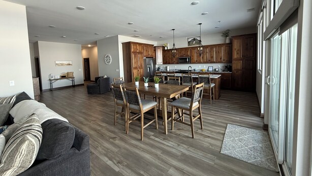 A spacious living room with a large wooden dining table and chairs, a gray sofa, and a kitchen area with wooden cabinets and a central island. - Spacious 2 bedroom condo on Lake Kampeska (Watertown)