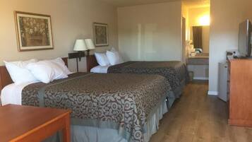 Ein Hotelzimmer mit zwei Betten, einem Holztisch, einem Schreibtisch, einem Fernseher und einem Badezimmer mit Spiegel und Waschbecken.