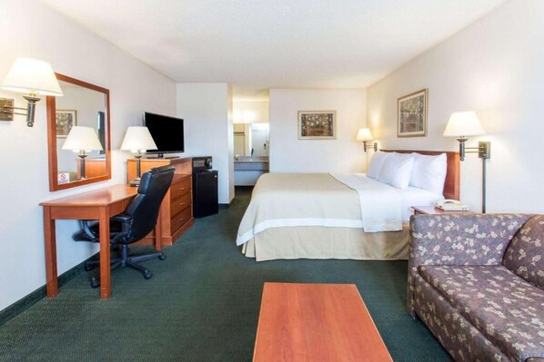 A hotel room with a bed, a desk with a chair, a sofa, a TV, and a mirror. - Travel Inn  (Mesa)