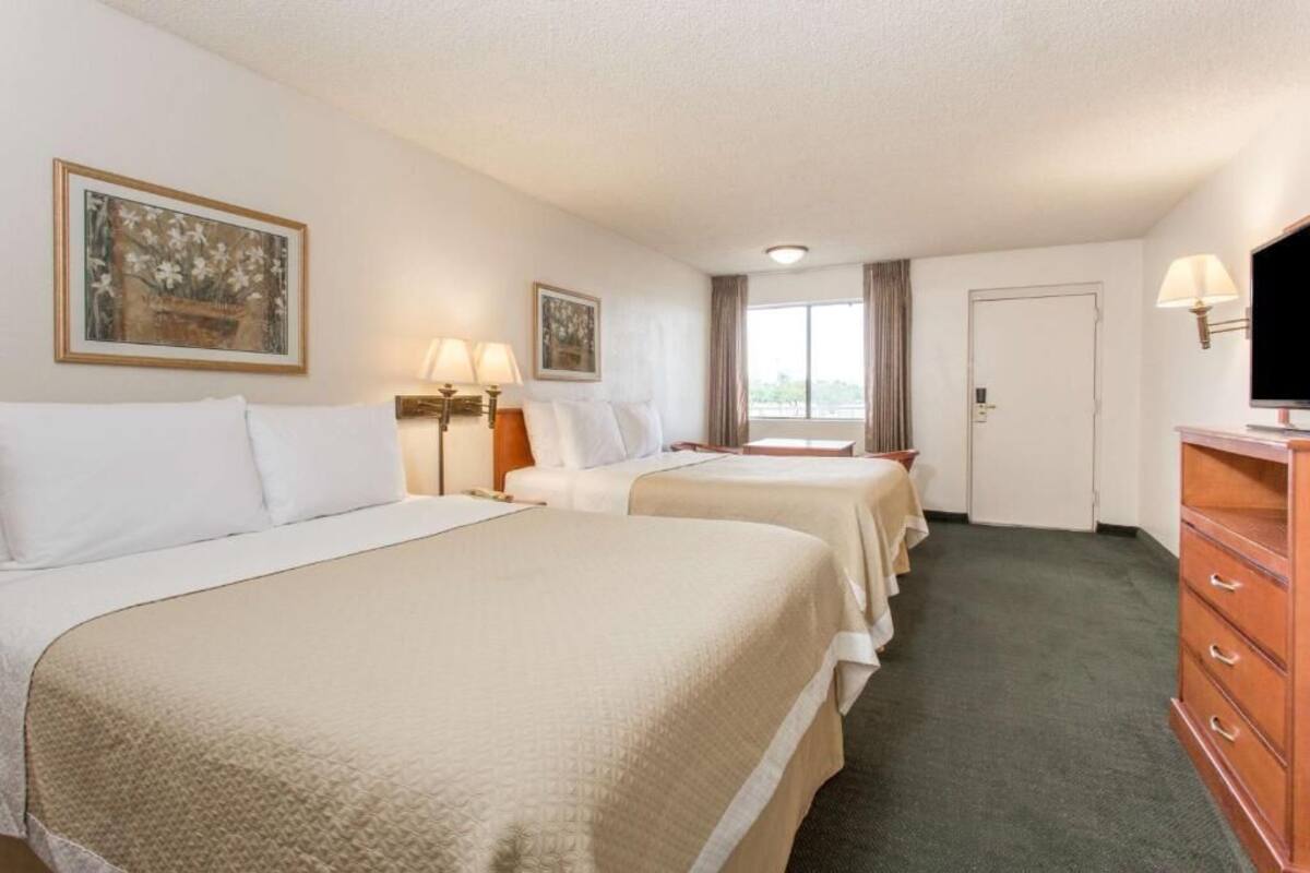 A hotel room with two beds, a dresser, a television, and a window with curtains.
