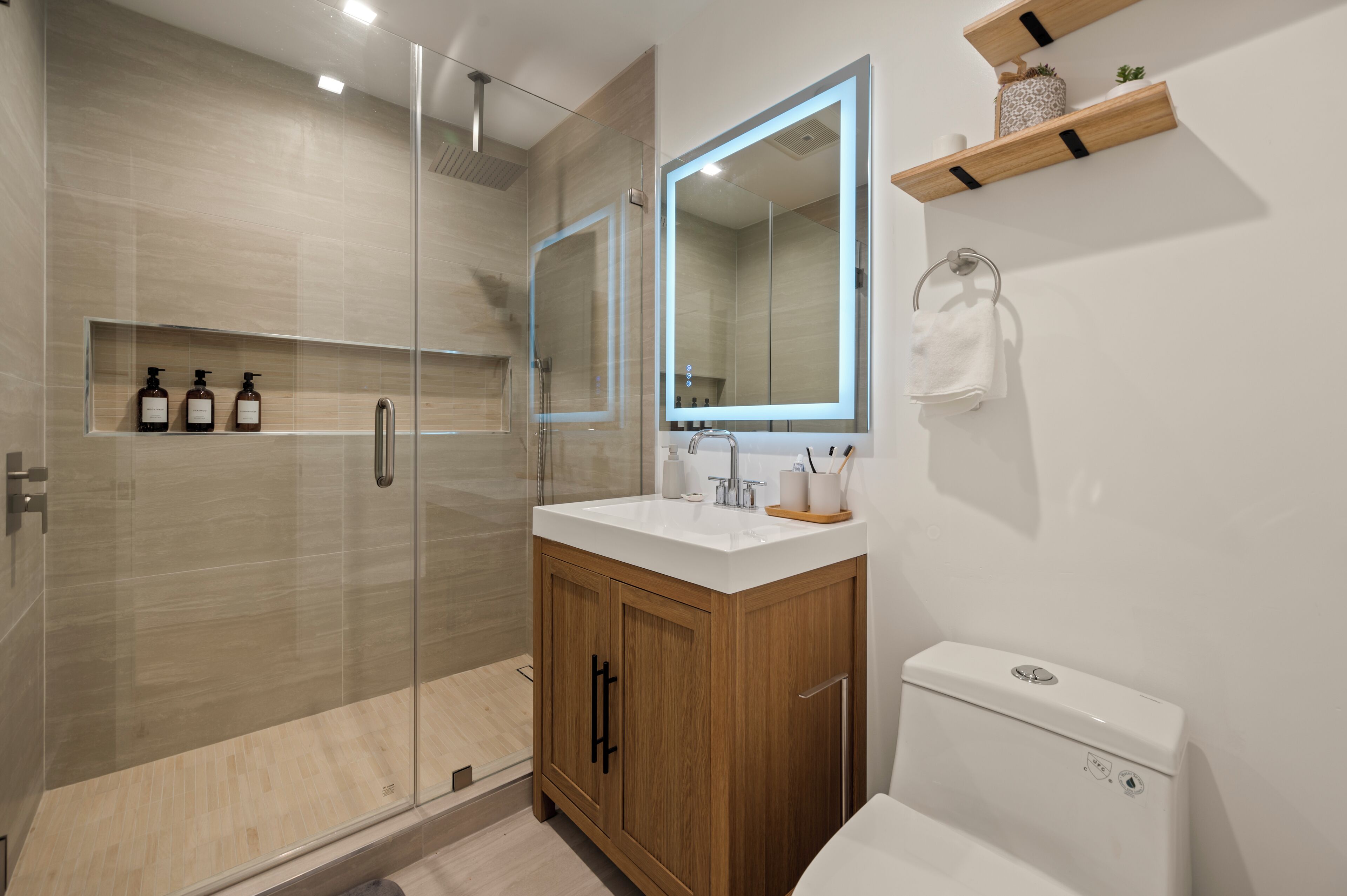 A modern bathroom with a glass-enclosed shower, a wooden vanity, and a large mirror.