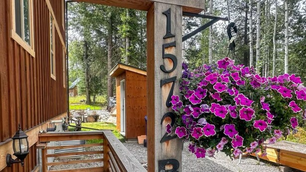 Una cabaña de madera con un letrero con el número '1577B' y una maceta colgante de flores.