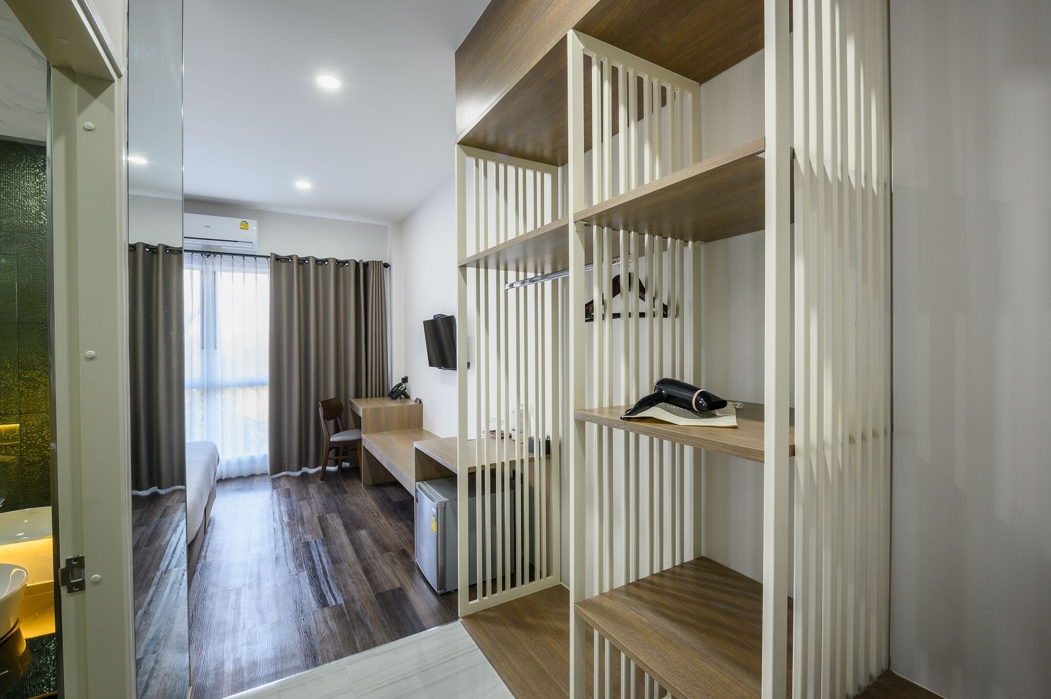 Una habitación de hotel moderna con piso de madera, una cama, un escritorio y un armario con listones verticales.