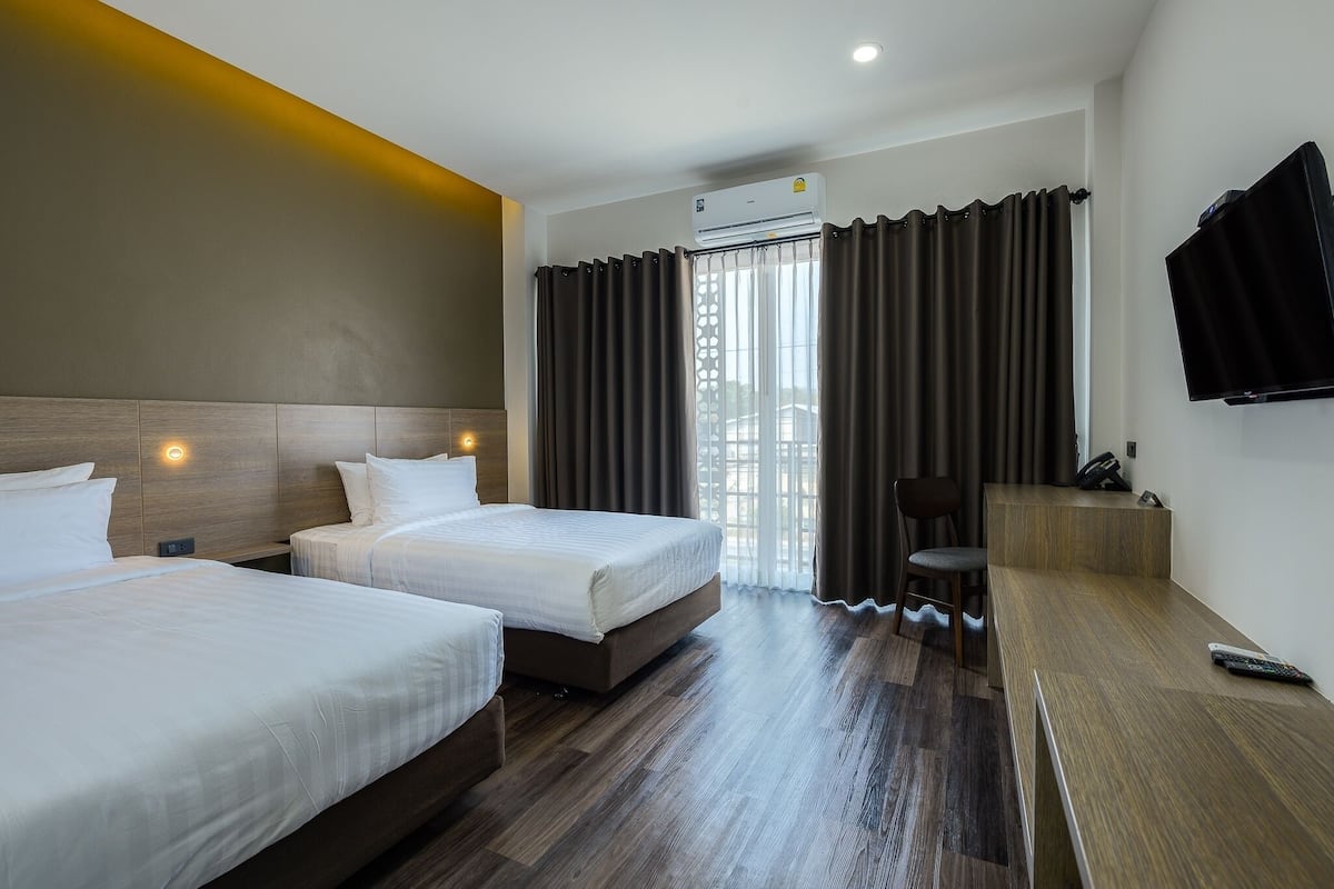 Een hotelkamer met twee bedden, een bureau, een stoel, een televisie en een airconditioning.