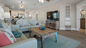 A living room with a sofa, coffee table, and TV. There is a kitchen in the background. - Beachfront, Tropical Paradise, Intimate Complex, EV Charger! (Indian Rocks Beach)