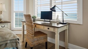 Un estudio con escritorio, computadora, lámpara y vista al océano a través de amplios ventanales.