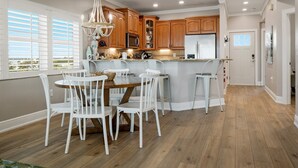 Una cocina moderna con armarios de madera, una isla central y un comedor con sillas blancas.