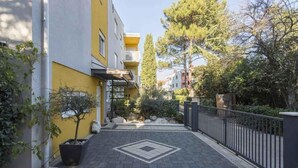 Uma trilha estreita leva a um edifício com fachada amarela, cercado por vegetação e uma grade de metal.