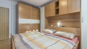 Quarto com cama, guarda-roupa de madeira e mesa de cabeceira.