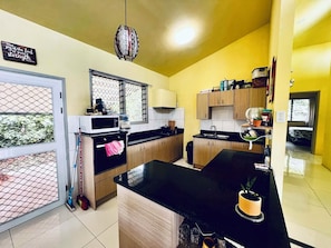 A kitchen with wooden cabinets, a black countertop, a microwave, and a hanging light fixture. - House of happiness/blessing (Apia)