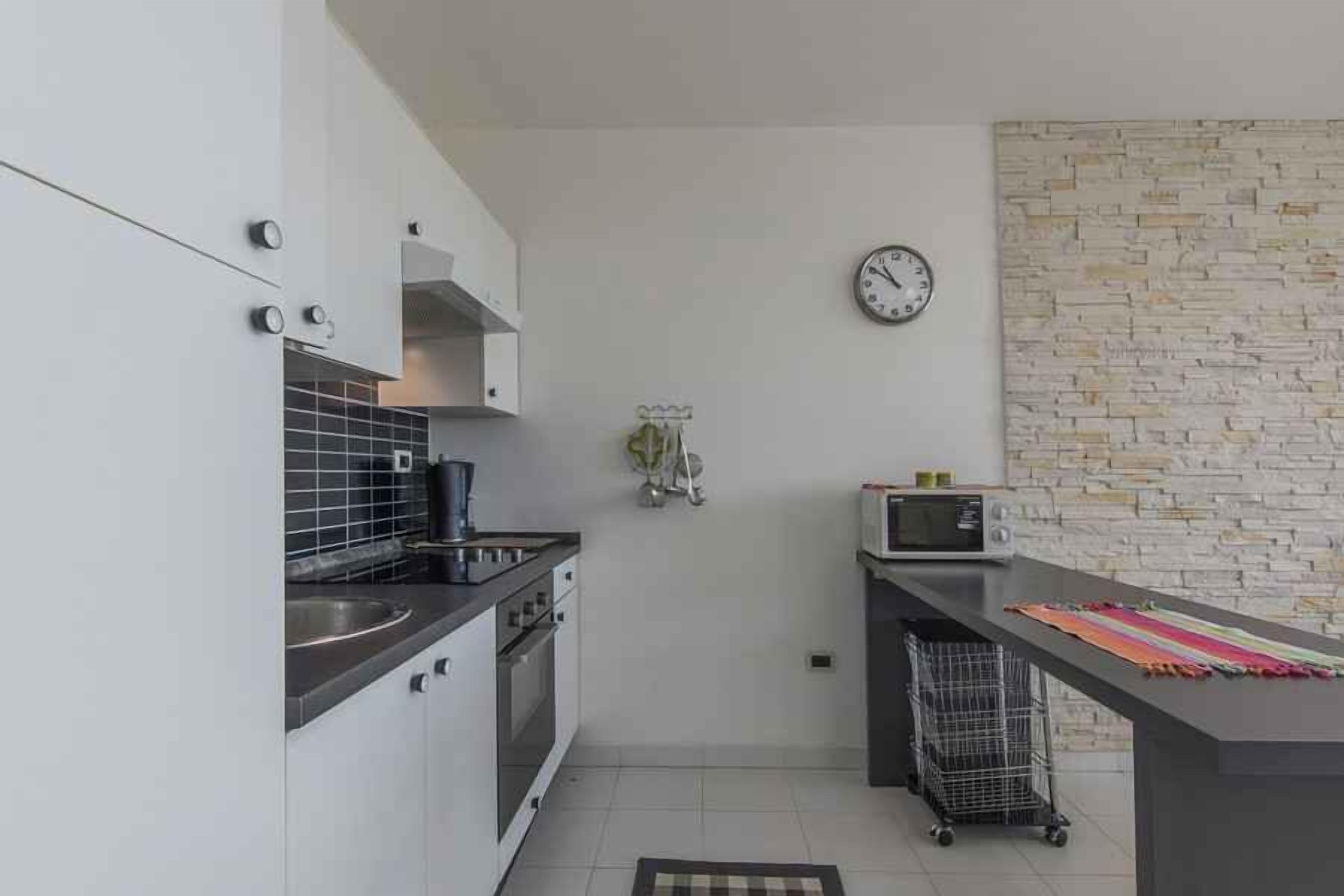 Une cuisine moderne avec des meubles blancs, un plan de travail noir, un four à micro-ondes et une horloge murale.