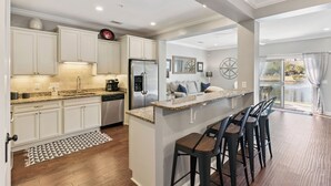 A modern kitchen with white cabinets, a granite countertop, and a built-in island with bar stools. - Coastal St. Simons Island Townhome Near Beaches, Shopping & Dining (Saint Simons Island)