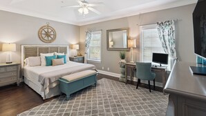 A bedroom with a bed, bedside tables, a desk, a chair, a ceiling fan, and a window with curtains. - Coastal St. Simons Island Townhome Near Beaches, Shopping & Dining (Saint Simons Island)