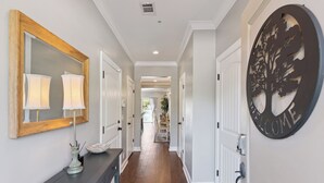 A hallway with a wooden-framed mirror, a blue console table with a lamp, and a welcome sign on the wall. - Coastal St. Simons Island Townhome Near Beaches, Shopping & Dining (Saint Simons Island)