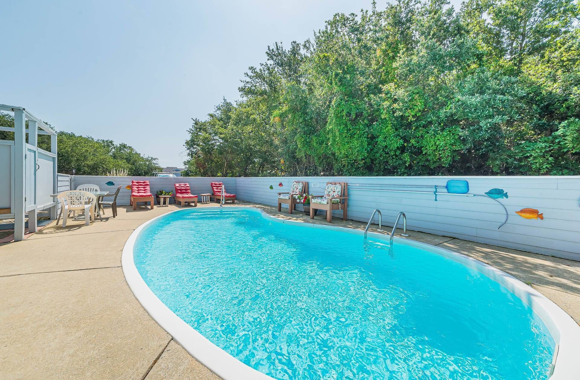 An outdoor swimming pool with lounge chairs and a white fence.