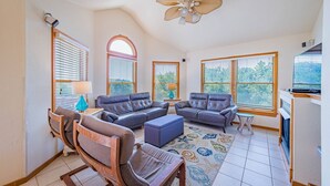 A spacious living room with a high ceiling, large windows, and a ceiling fan. - Knot A Care - Corolla, Ocean Sands, 400 Yds to Beach, Pool, Hot Tub, Pool Table, Pets OK (Corolla)