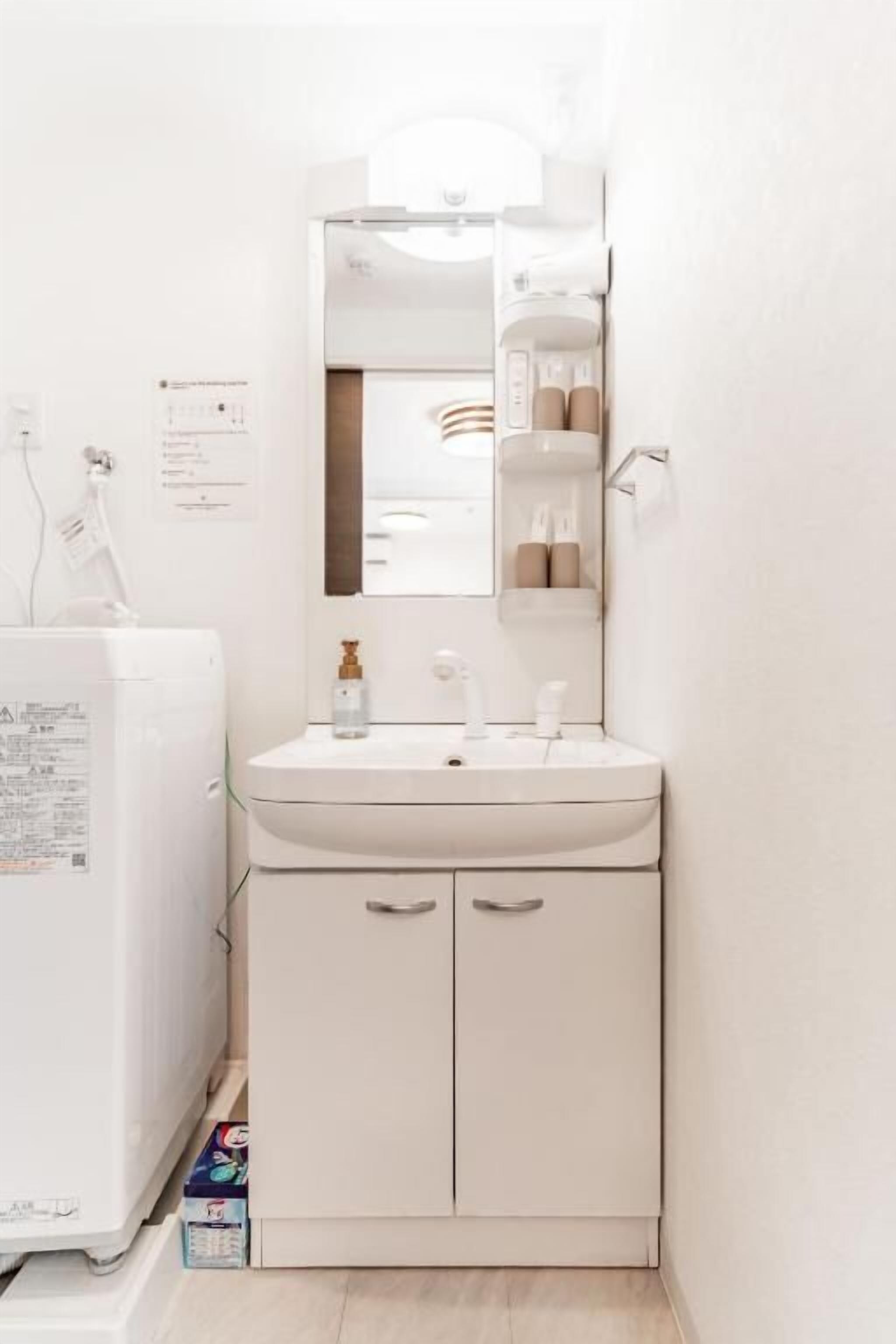 A small, white bathroom with a sink, mirror, and cabinets. There is a white heater or appliance to the left of the sink.