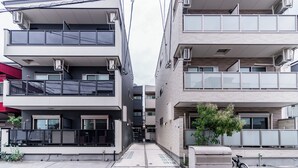 A modern multi-story residential building with balconies, air conditioning units, and a narrow pedestrian pathway. - Chuan House Asahi (Osaka)