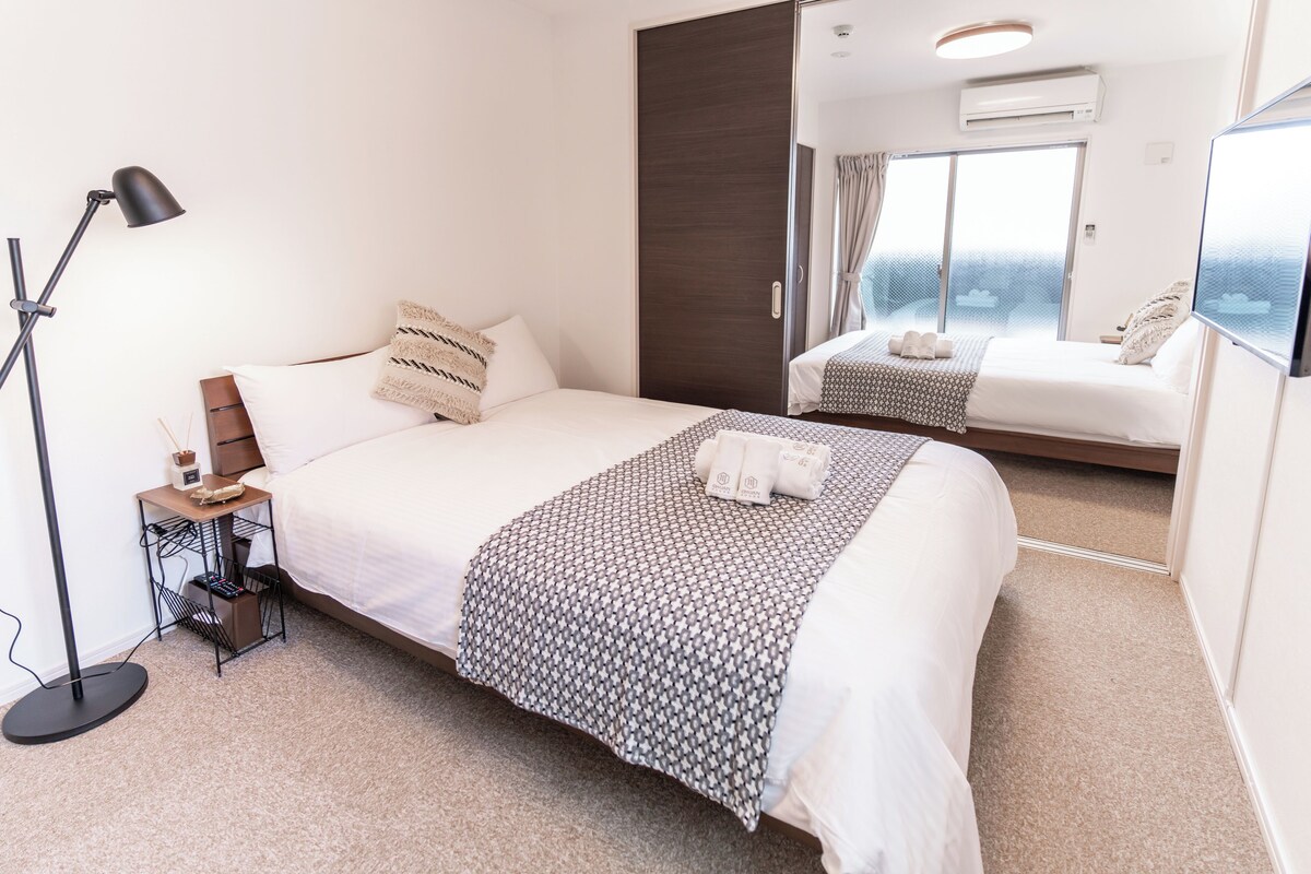 A hotel room with a large bed, a bedside table with a lamp, a small side table, and a large mirror.