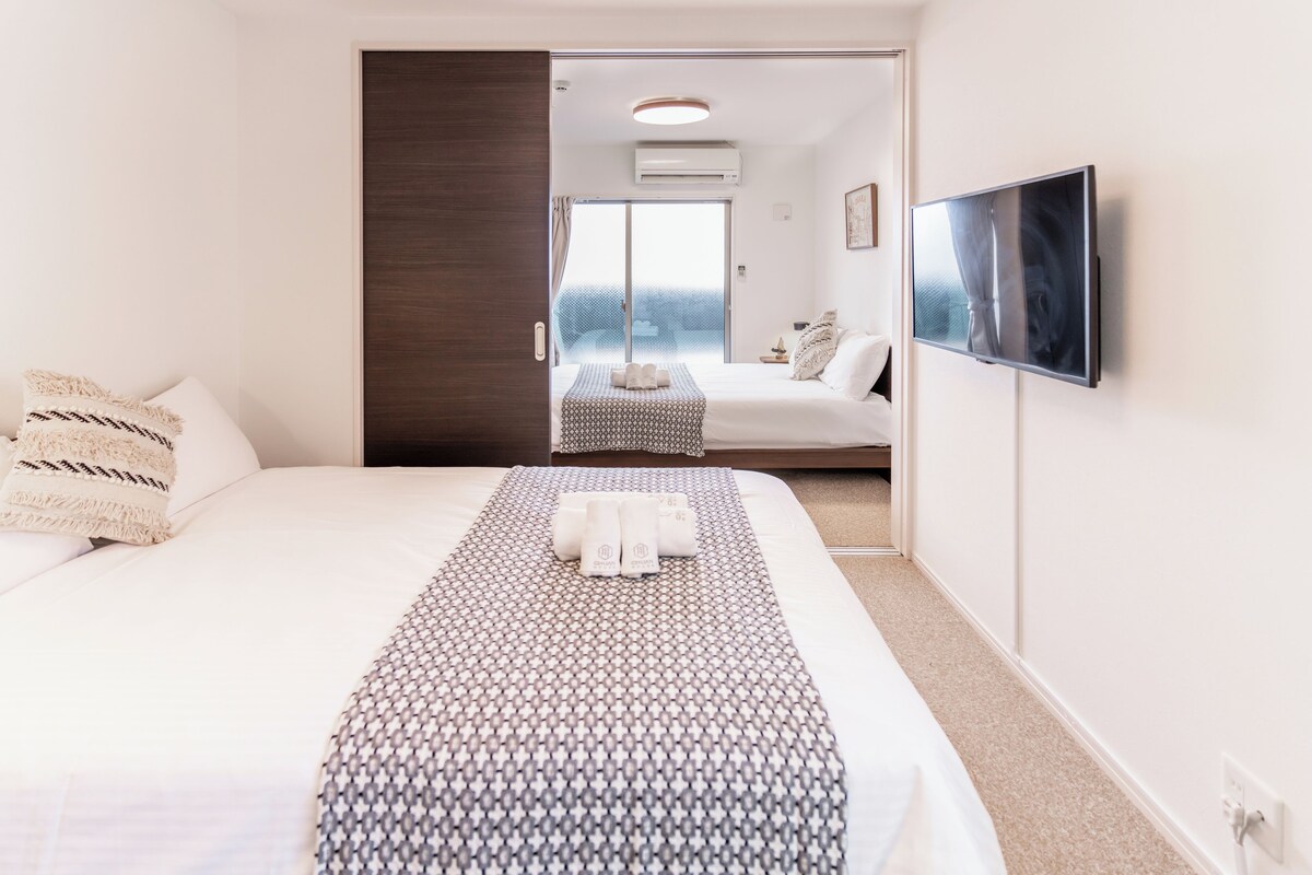 A hotel room with a large bed, a TV mounted on the wall, and a sliding door leading to a balcony.