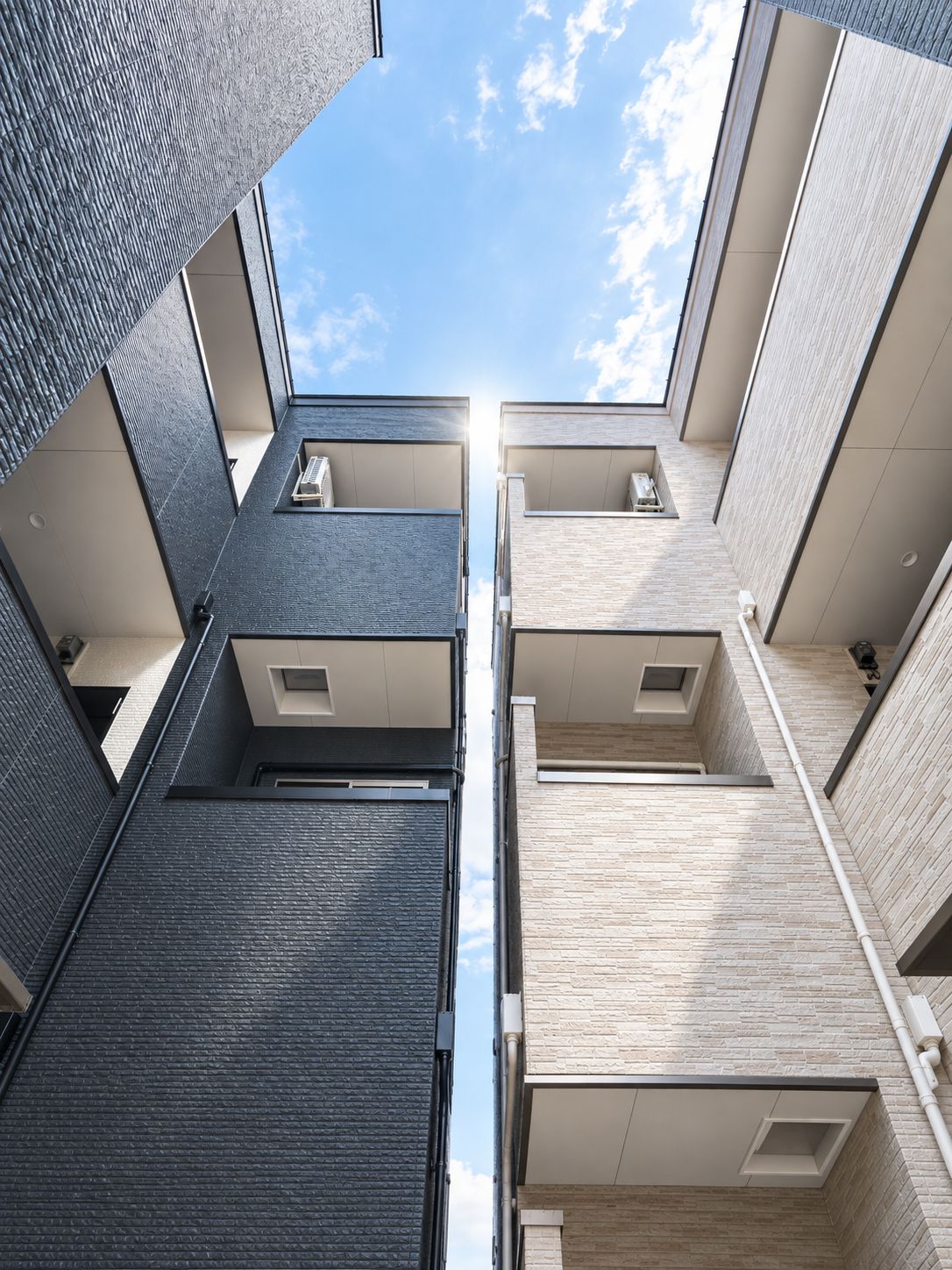 A modern building with a central atrium, multiple balconies, and a clear sky view.