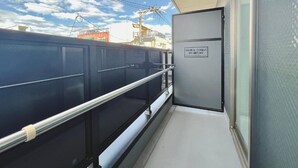 A balcony with a glass barrier, a door with a sign, and a view of buildings and power lines. - Chuan House Asahi (Osaka)