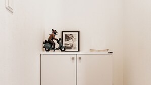 A white cabinet with two doors, a small shelf with a figurine and a framed picture, and a light switch on the wall. - Chuan House Asahi (Osaka)