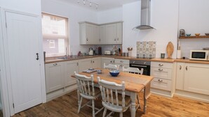 A compact kitchen with white cabinets, a wooden dining table, two chairs, a microwave, and a stove. - The English School, Flat 2 (Dartmouth)