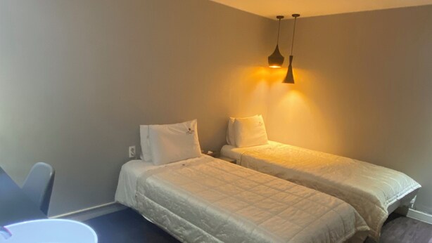 Une chambre avec deux lits, un bureau avec une lampe et un luminaire au plafond.