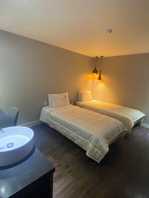 Une chambre avec deux lits, un bureau avec une lampe et un luminaire au plafond.