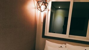 Une chambre d’hôtel avec un lit, des oreillers, un luminaire fixé au mur et une fenêtre.