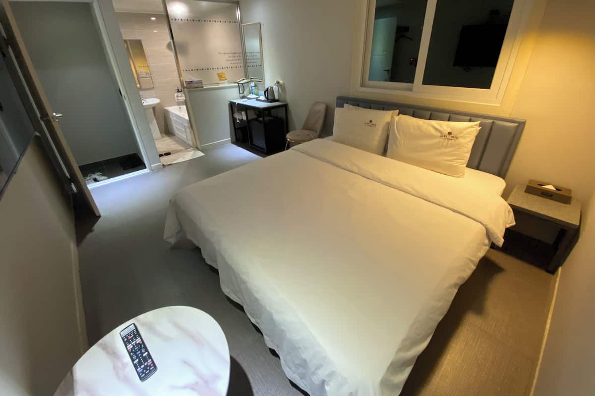 A hotel room with a large bed, a desk, a chair, a mirror, and a window.