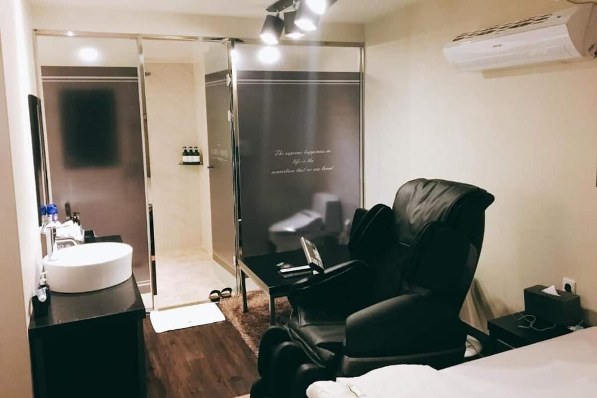 A modern hotel room with a round white sink, a black leather chair, a small table, and a bed.