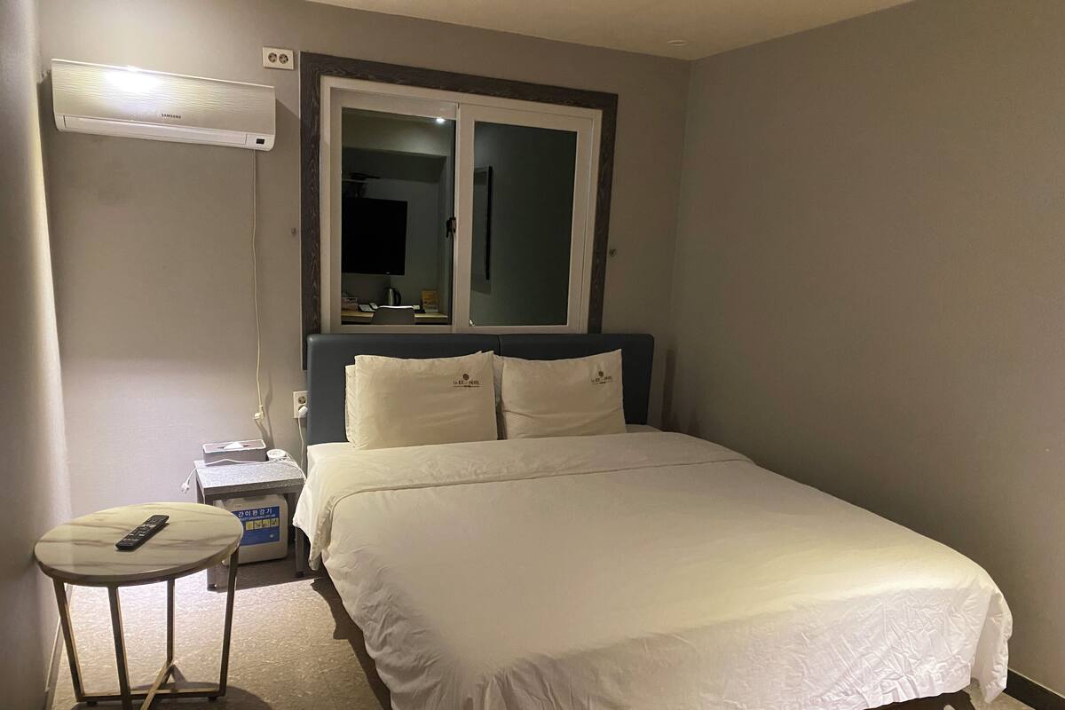 A hotel room with a bed, bedside table, lamp, and a window with a view.