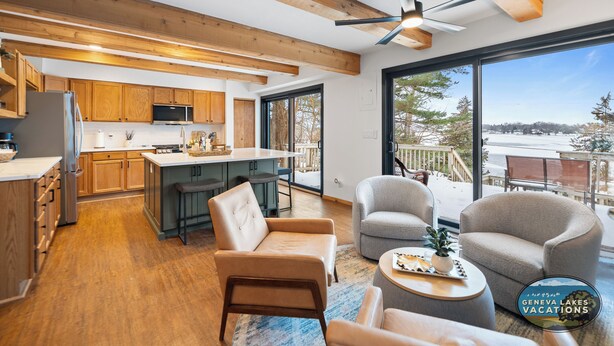 A modern kitchen with wooden beams, a large island, and a view of a snowy landscape through large windows. - Lakefront Getaway, Swim, Laugh, Family Fun for all! Close to Kettle Moraine (Palmyra)