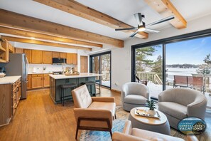 Een moderne keuken met houten balken, een groot keukeneiland en uitzicht op een besneeerd landschap door grote ramen.
