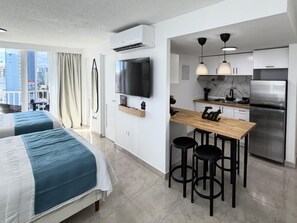 A modern hotel room with two beds, a kitchen area with a refrigerator, and a TV mounted on the wall. - Refined apartment with partial ocean-view balcony, steps from Condado Beach. (San Juan)