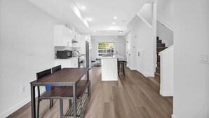A modern kitchen with white cabinetry, a central island, and a dining area with a wooden table and chairs. - Crescent Heights Escape (Calgary)