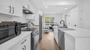 A modern kitchen with white cabinetry, stainless steel appliances, and a central island. - Crescent Heights Escape (Calgary)