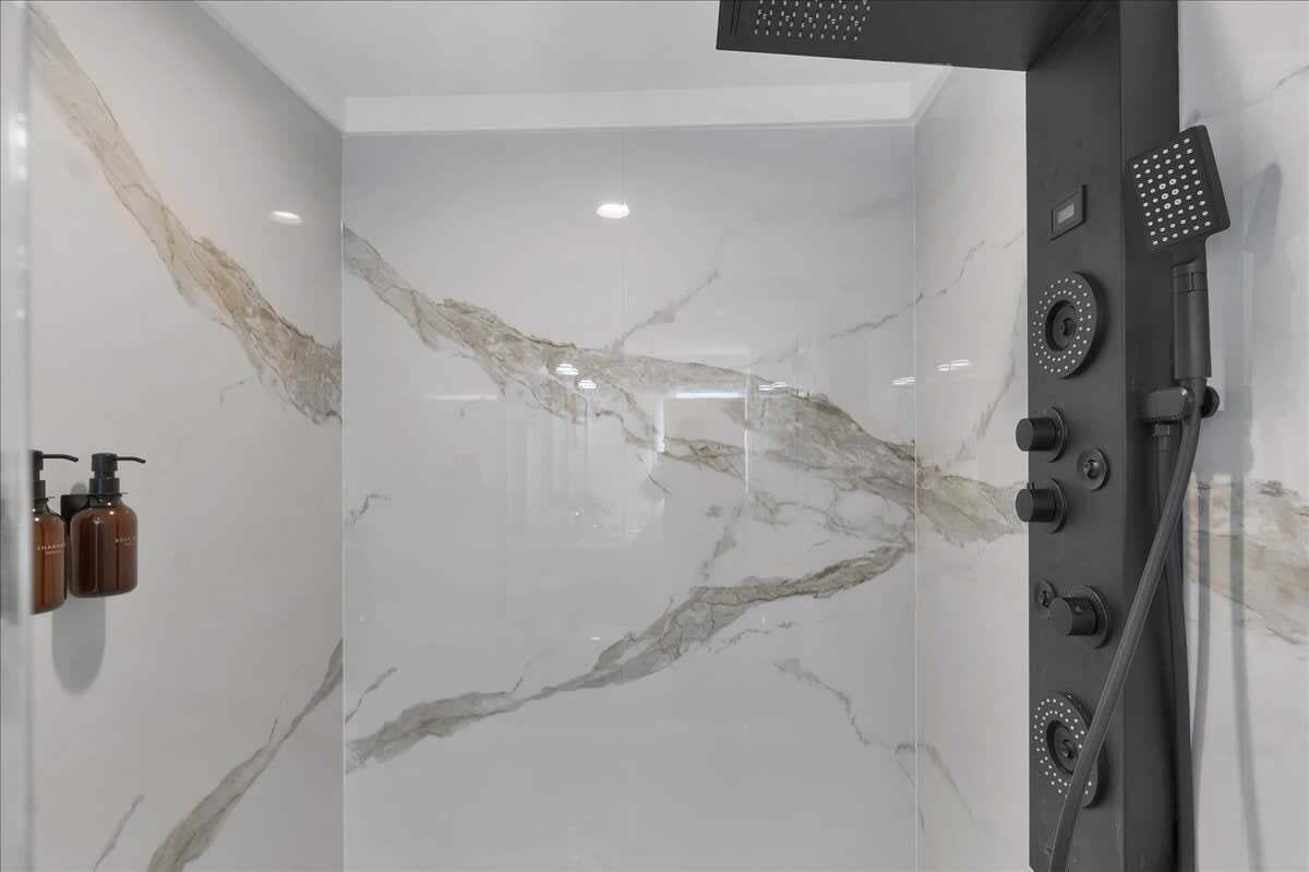 A modern bathroom with a glass shower enclosure, marble walls, and a black showerhead.
