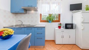 Una cucina compatta con mobili azzurri, un frigorifero bianco, un forno a microonde e un tavolino con una ciotola di frutta.