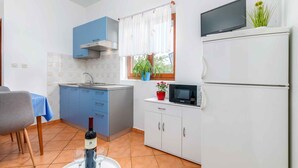 Una cucina compatta con mobili blu, un forno a microonde, un frigorifero, un lavello e un angolo pranzo con tavolo e sedie.