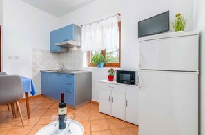 A compact kitchen with blue cabinets, a microwave, a refrigerator, a sink, and a dining area with a table and chairs. - Holiday apartment mit Klimaanlage (Fažana)