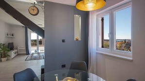 Ein modernes Wohnzimmer mit einem Glastisch, einem großen Fenster mit Blick, einer Wanduhr und einer Treppe, die in eine obere Ebene führt.