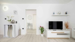 Ein modernes Wohnzimmer mit einer weißen Unterhaltungsecke, einem Flachbildfernseher und einer kleinen Ablagefläche mit Dekoration.